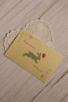 Front view of the 4 x 6 inch birthday postcard featuring a black pixel-style rabbit reaching towards a red strawberry on a soft yellow dotted background.