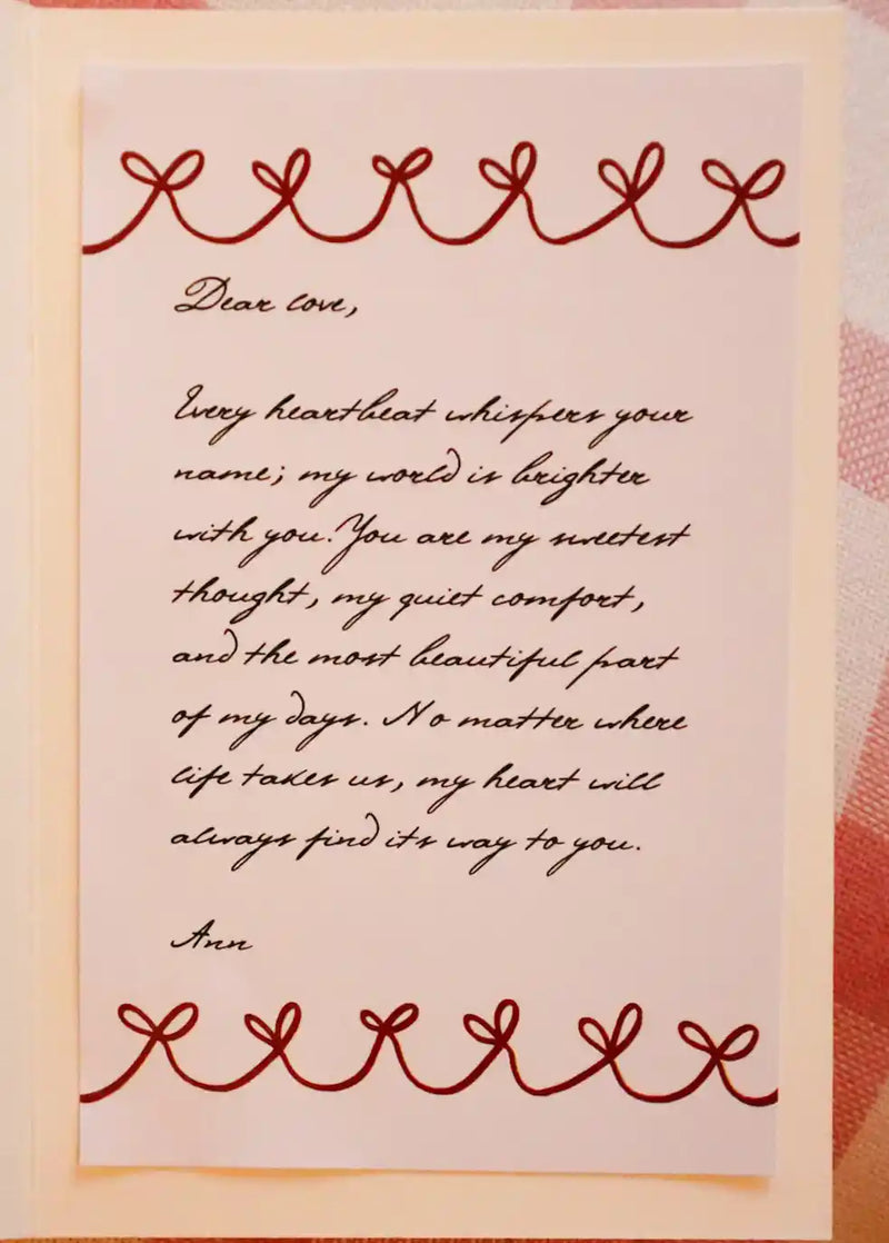 An open pink greeting card with a red ribbon border laid on a pink gingham cloth, showing a customer's long personalised message handwritten in script inside the card.