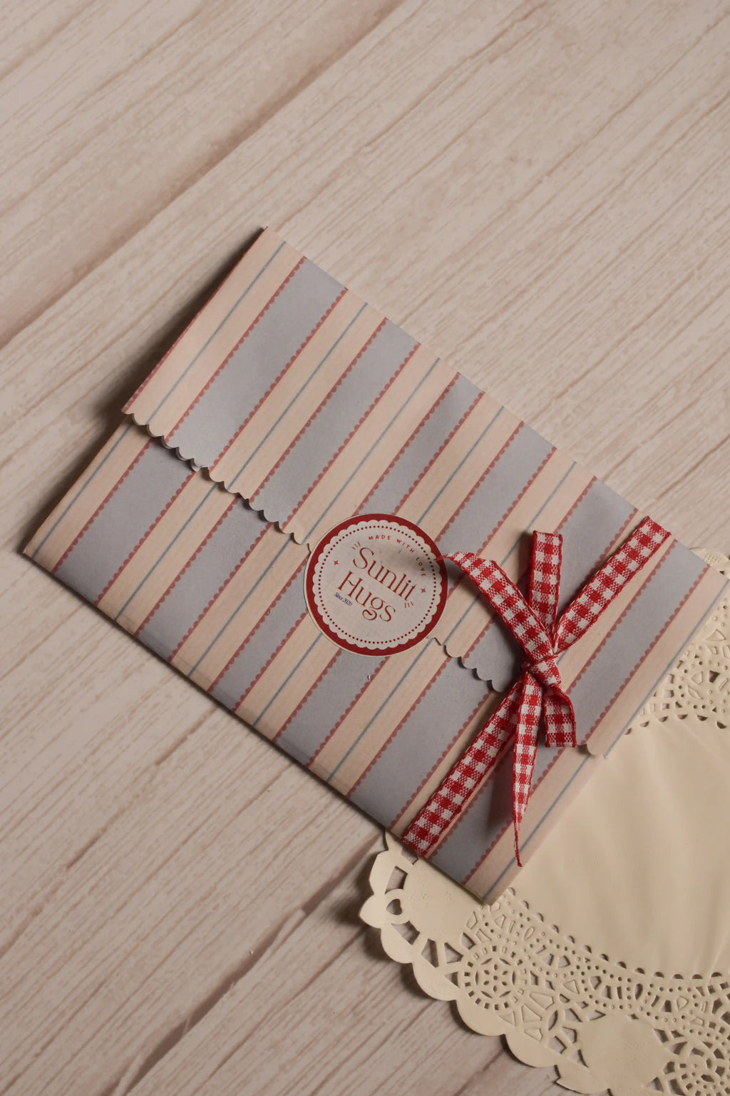 The Little Birthday Magic Postcard Set presented inside a cream, blue and red striped paper sleeve with scalloped edges, a Sunlit Hugs label and a red gingham ribbon.