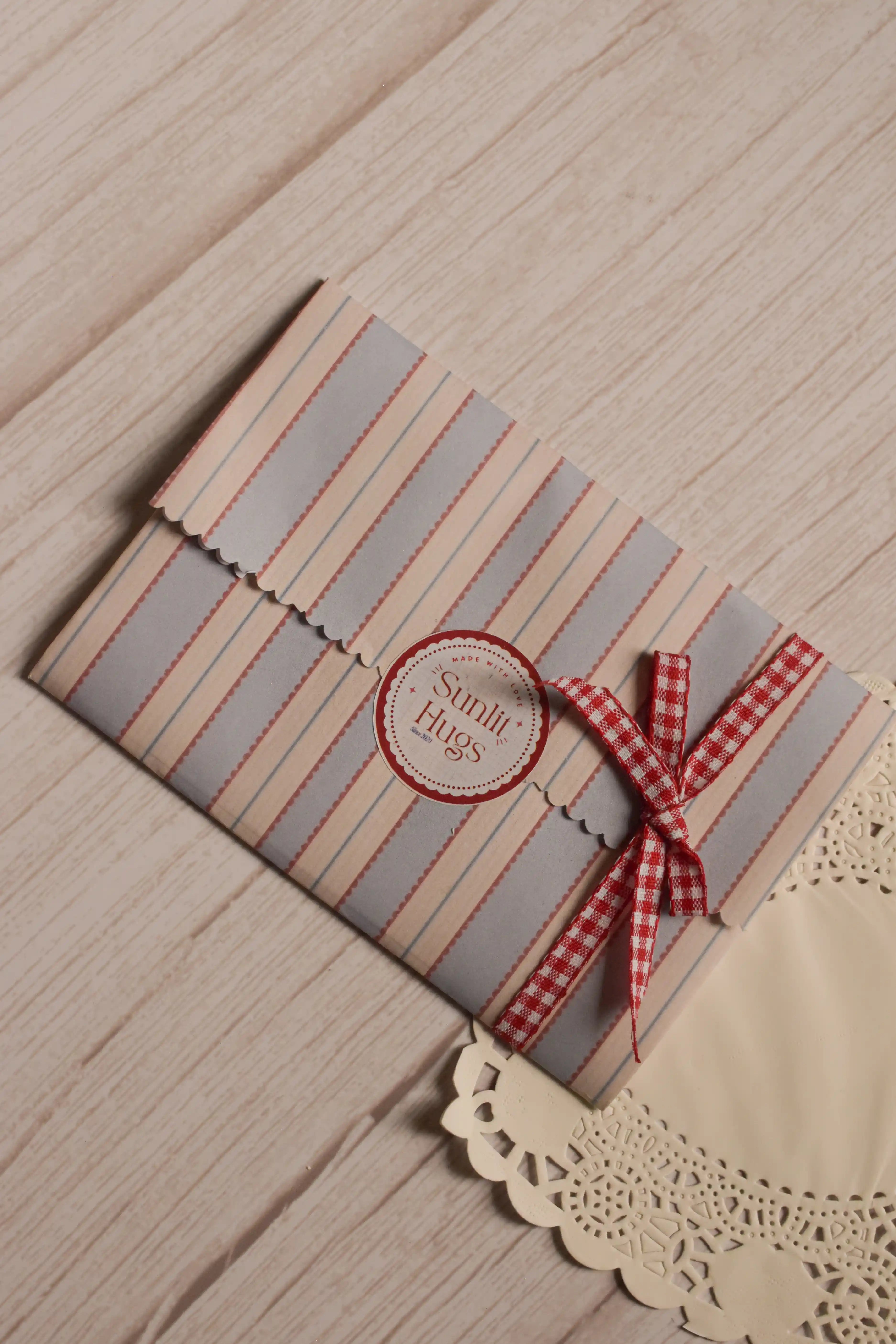 The Little Birthday Magic Postcard Set presented inside a cream, blue and red striped paper sleeve with scalloped edges, a Sunlit Hugs label and a red gingham ribbon.