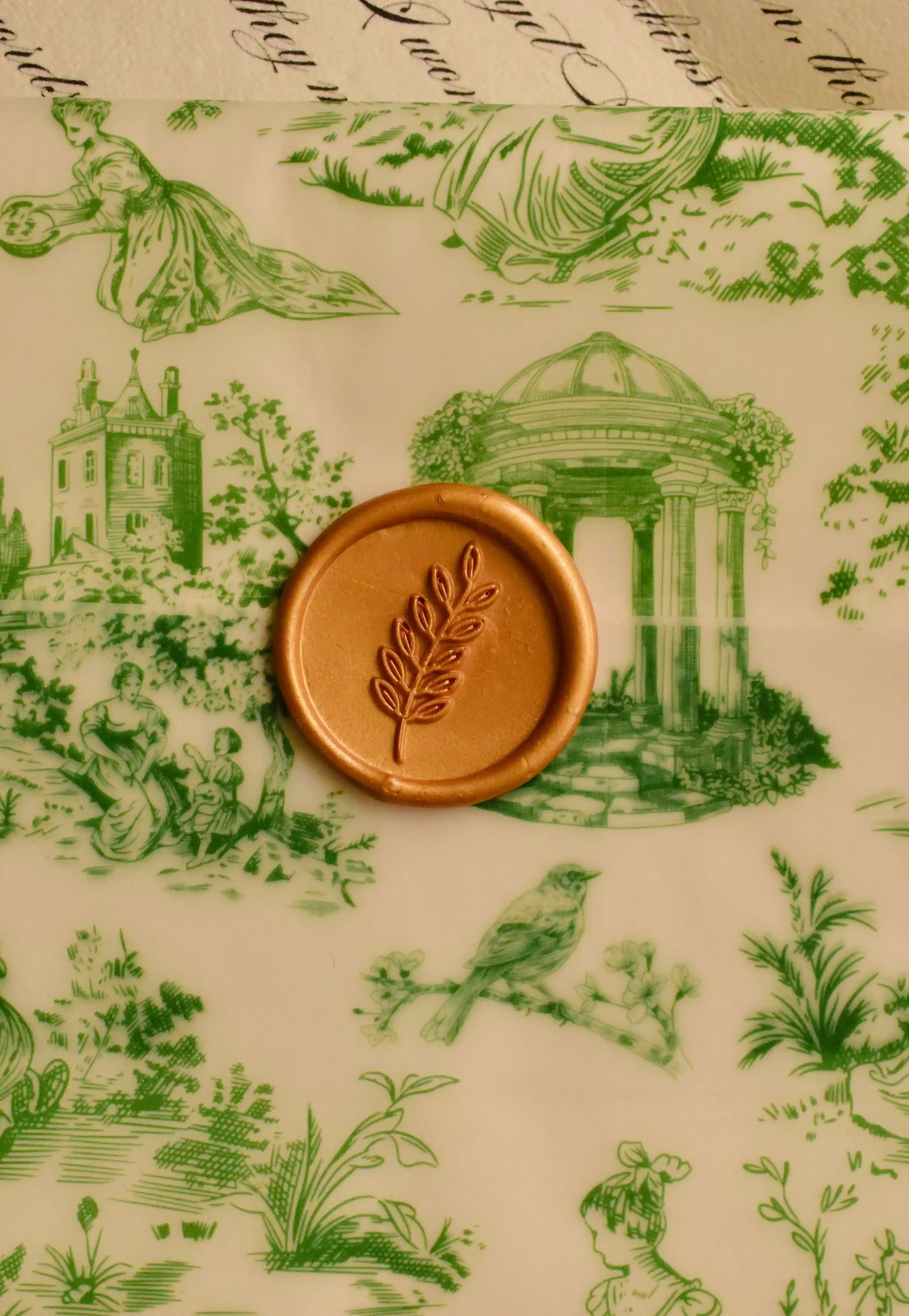 A detailed view highlighting the rich golden wax seal and its delicate leaf design, showcasing the meticulous craftsmanship over the green toile architectural print.