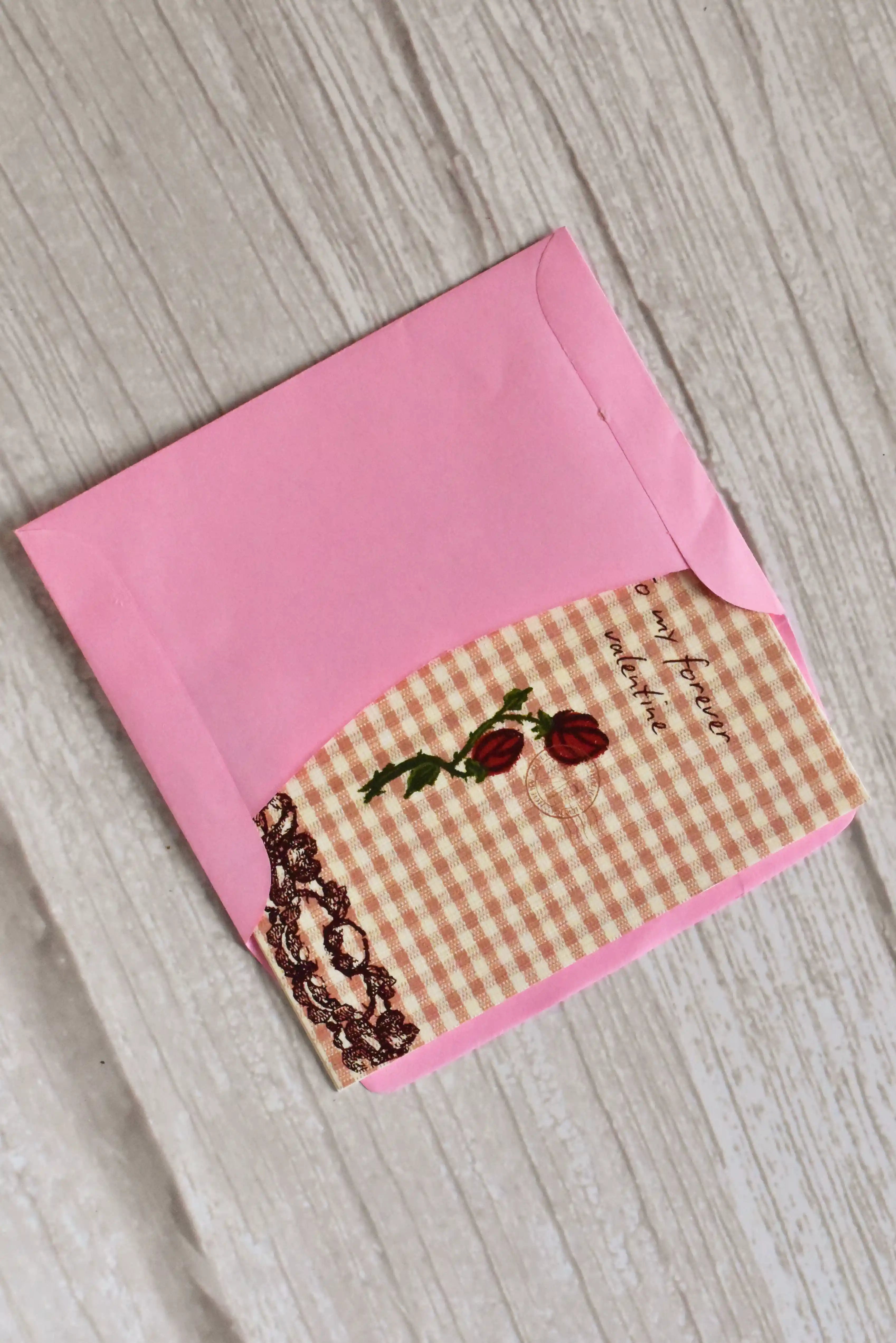 A vintage gingham mini Valentine card with roses is styled on a warm wooden surface.