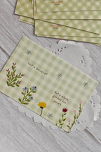 A cottagecore green gingham garden postcard is shown with flower illustrations.