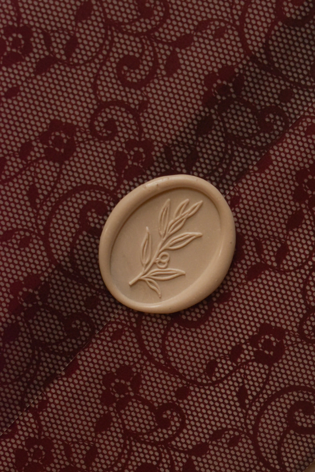 Detailed close-up showing the ivory botanical wax seal against the intricate burgundy floral lace pattern of Rosie's translucent vellum wrapper.