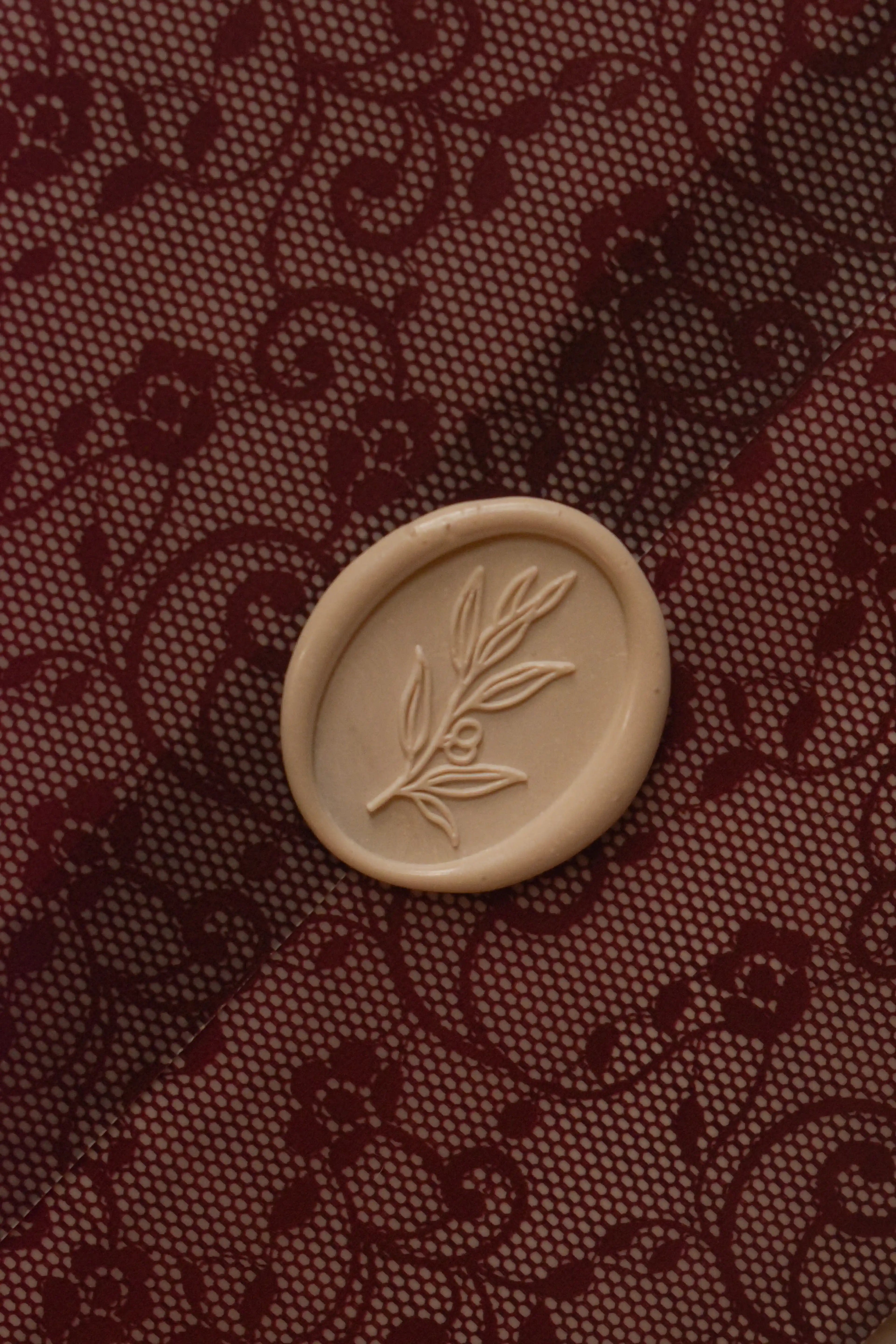 Detailed close-up showing the ivory botanical wax seal against the intricate burgundy floral lace pattern of Rosie's translucent vellum wrapper.