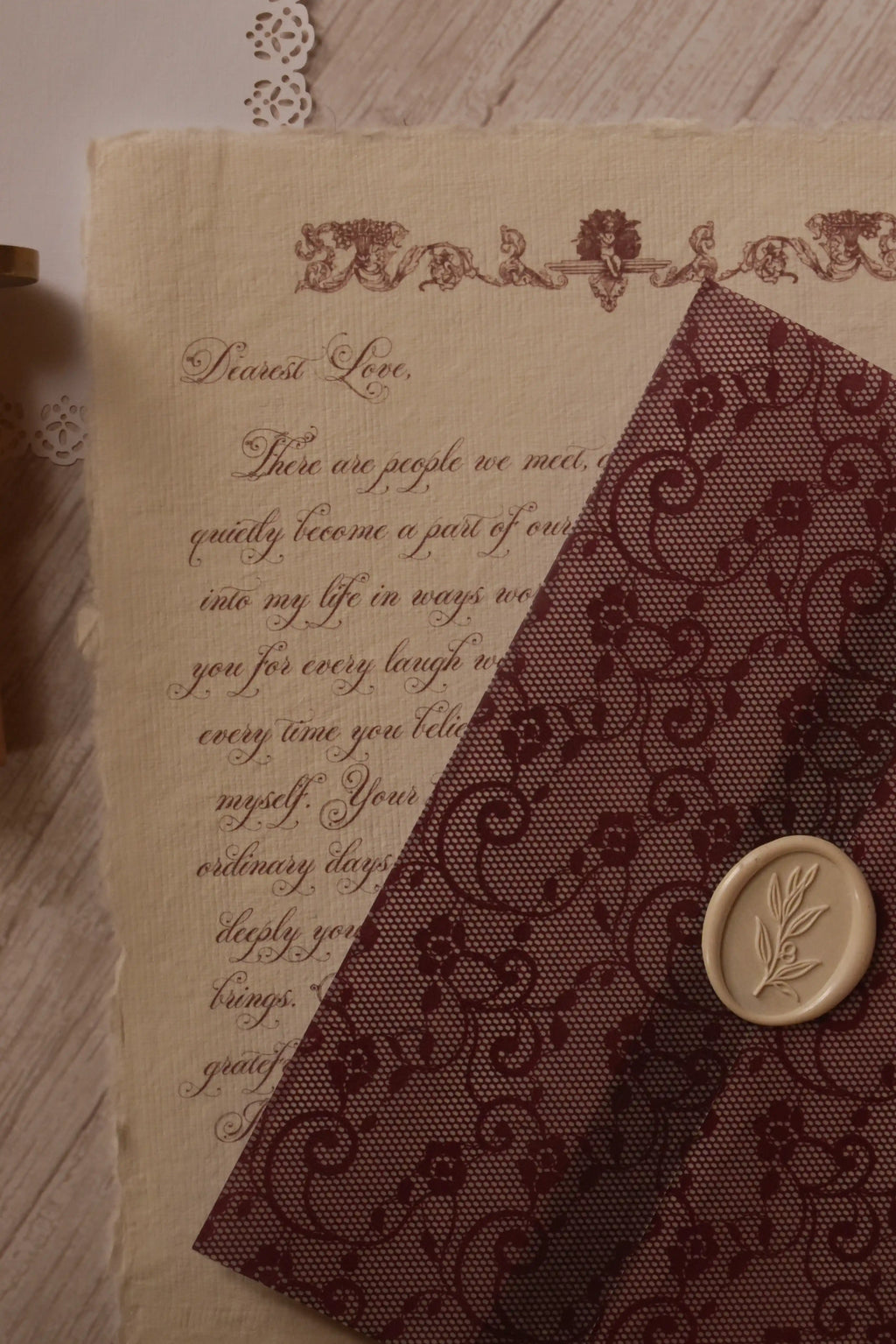 A Rosie vintage letter on ivory handmade paper displayed beside a burgundy lace-patterned vellum wrapper finished with an ivory botanical wax seal.