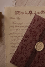 A Rosie vintage letter on ivory handmade paper displayed beside a burgundy lace-patterned vellum wrapper finished with an ivory botanical wax seal.