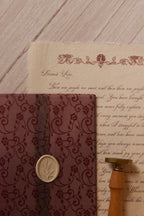 Vintage stationery arrangement featuring the Rosie personalised letter on textured handmade paper beside its burgundy lace-patterned vellum wrapper and wax seal accessories.