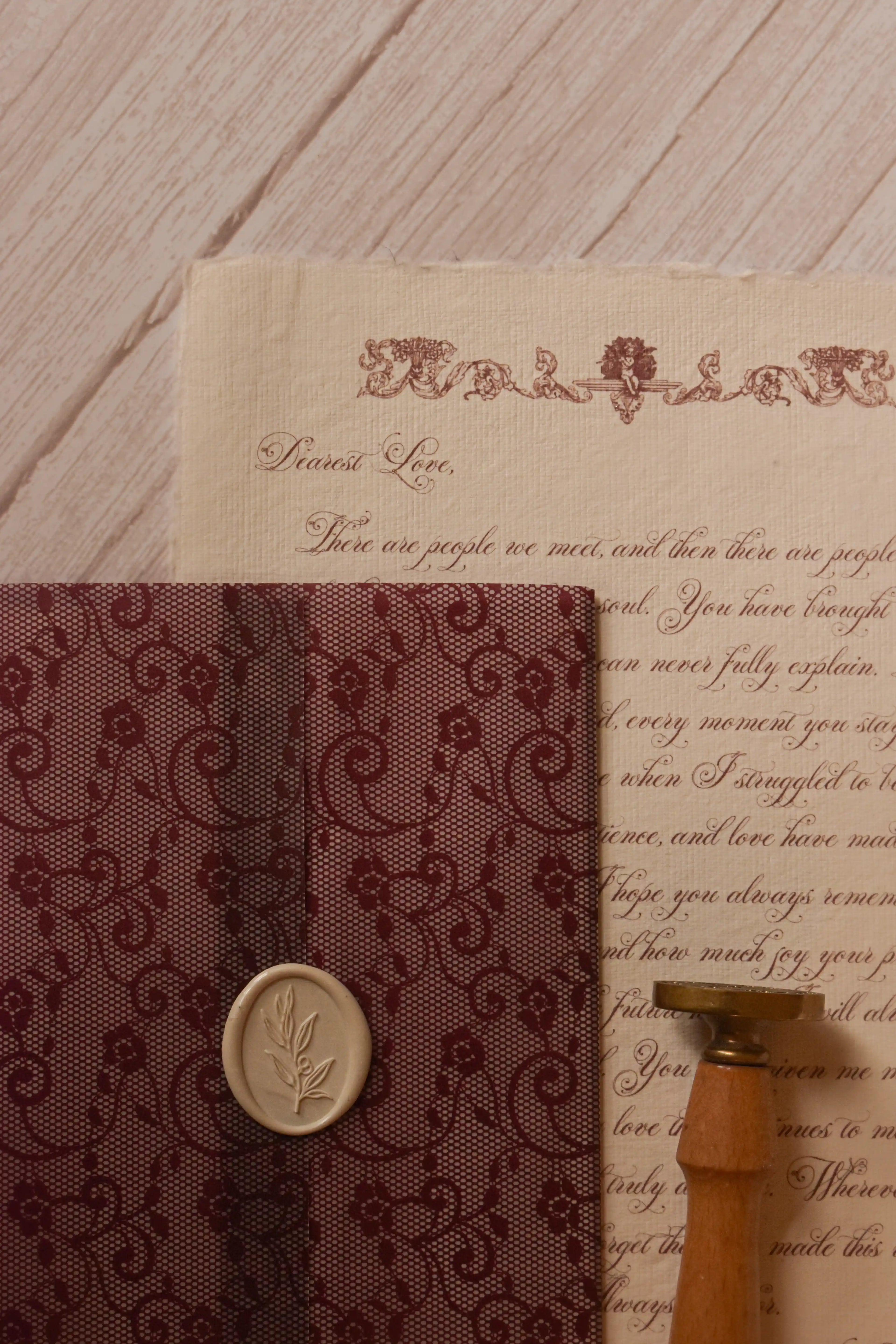 Vintage stationery arrangement featuring the Rosie personalised letter on textured handmade paper beside its burgundy lace-patterned vellum wrapper and wax seal accessories.