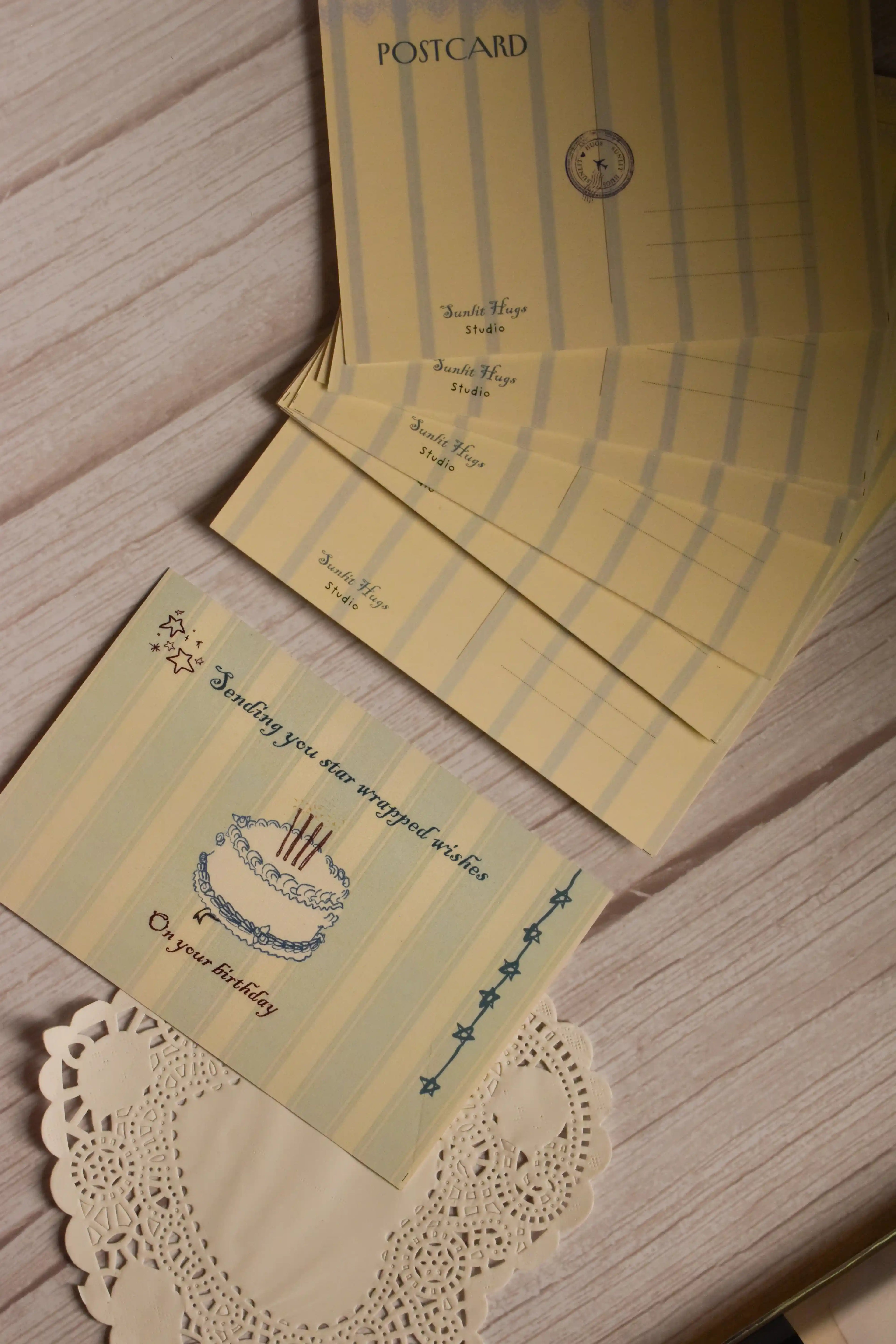 A styled arrangement showing both sides of the Star-Wrapped Wishes Birthday Postcard. The front features a cake and celestial birthday message, while the back includes a classic striped postcard layout.