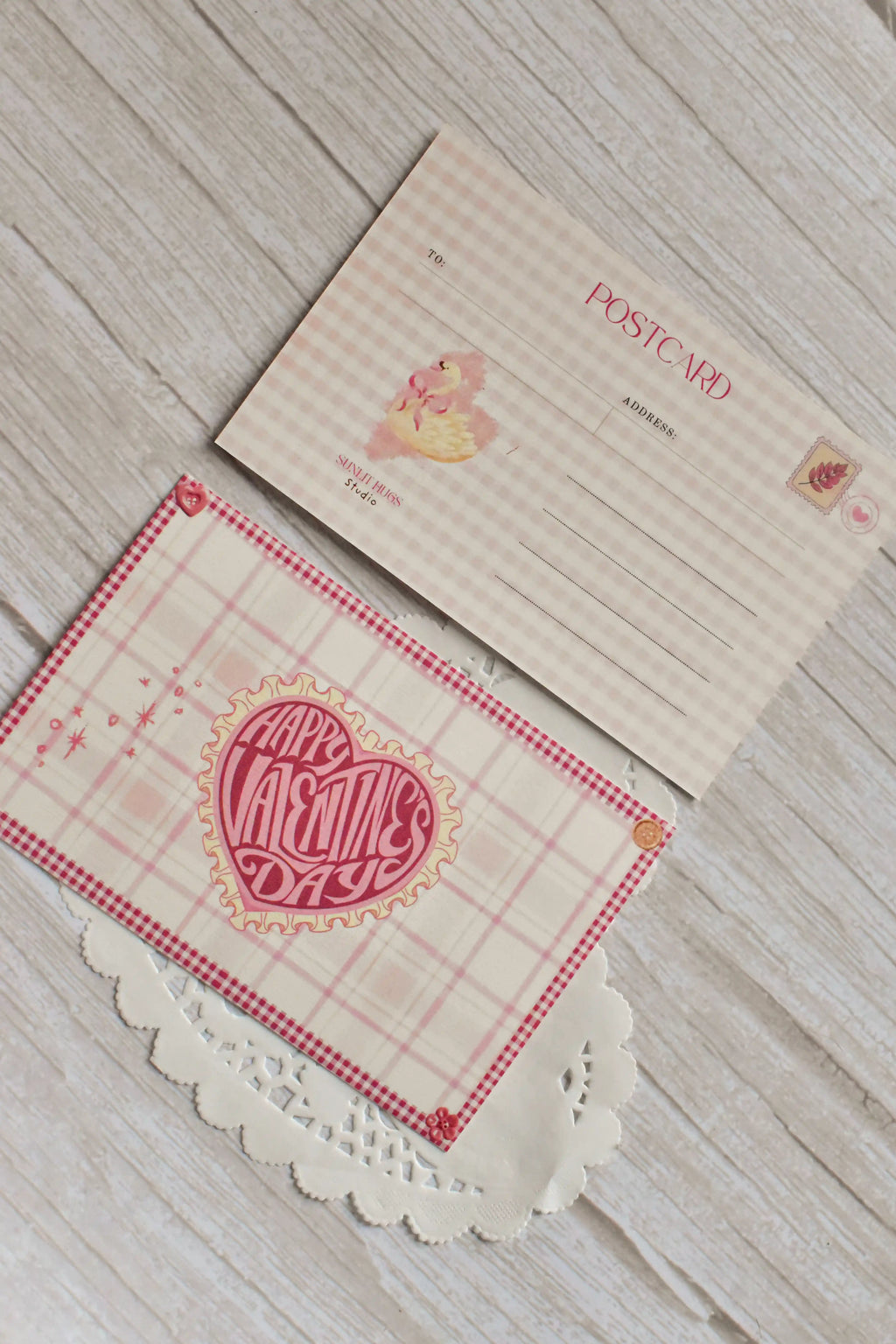 A pink gingham Valentine postcard shows vintage heart and swan artwork on a tabletop.