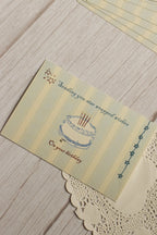 Close-up view highlighting the illustrated birthday cake, celestial stars, soft striped background and the message “Sending you star wrapped wishes on your birthday.”