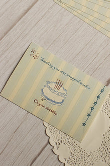 Close-up view highlighting the illustrated birthday cake, celestial stars, soft striped background and the message “Sending you star wrapped wishes on your birthday.”