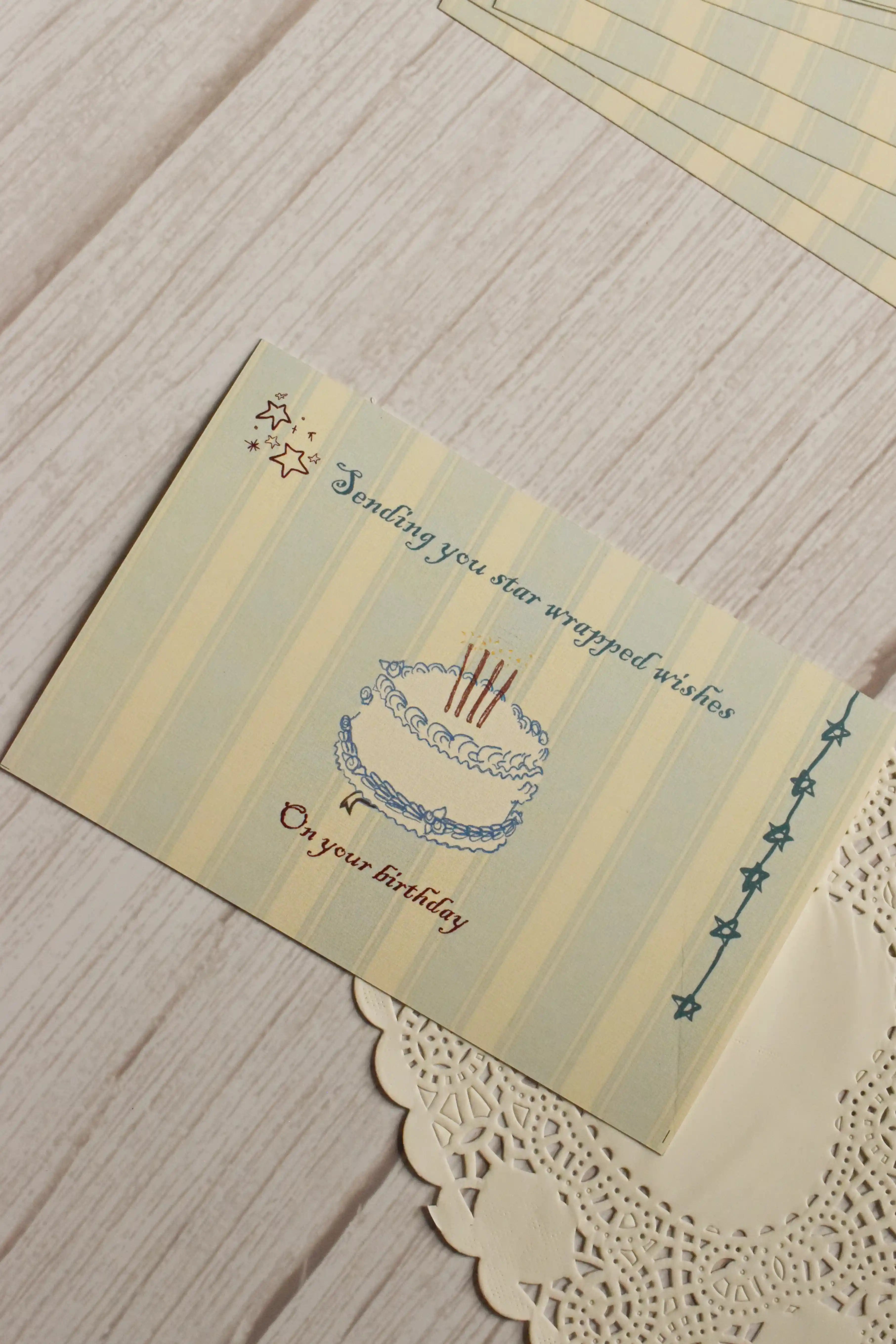 Close-up view highlighting the illustrated birthday cake, celestial stars, soft striped background and the message “Sending you star wrapped wishes on your birthday.”