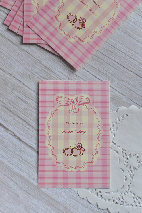 A pink gingham postcard shows retro cherries, bows, and the message You Make My Heart Sing.
