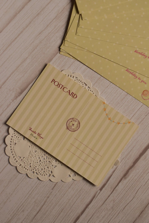 Back view of the postcard featuring cream vertical stripes, a red POSTCARD heading, writing lines, a circular postal-style mark and a small yellow star garland.