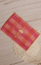 Angled close-up of the postcard front featuring a hanging jellyfish, tiny celestial details and the phrase “You fill this world with so much magic” over a coral and pink checkered design.