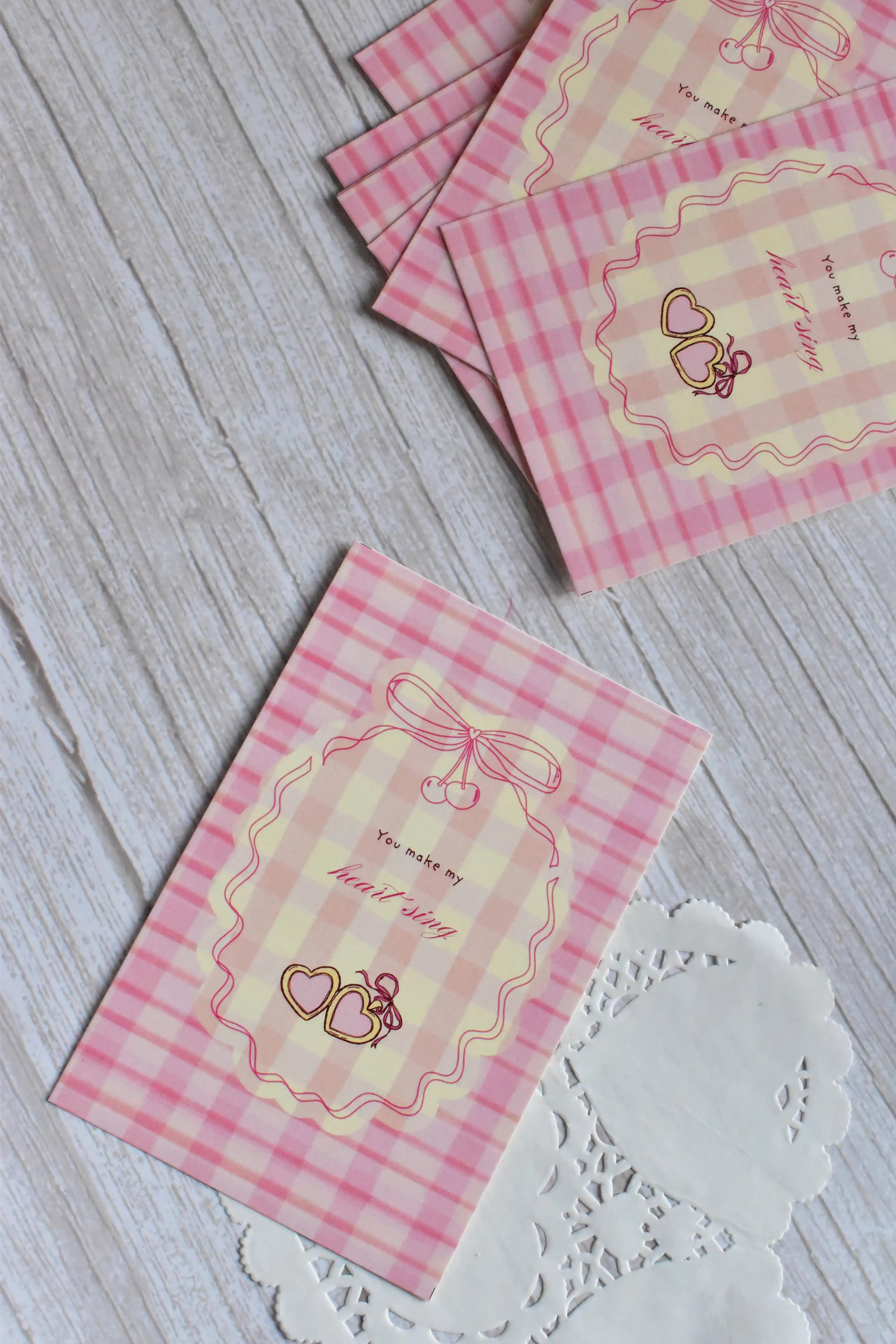 A Valentine postcard with pink gingham, red cherries, and bow accents is shown in a romantic flat lay.