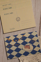 Front and back view of the 4 x 6 inch You’re Full of Whimsy Birthday Postcard featuring a blue and cream harlequin pattern, birthday cake, golden stars and a vintage-inspired writing side.